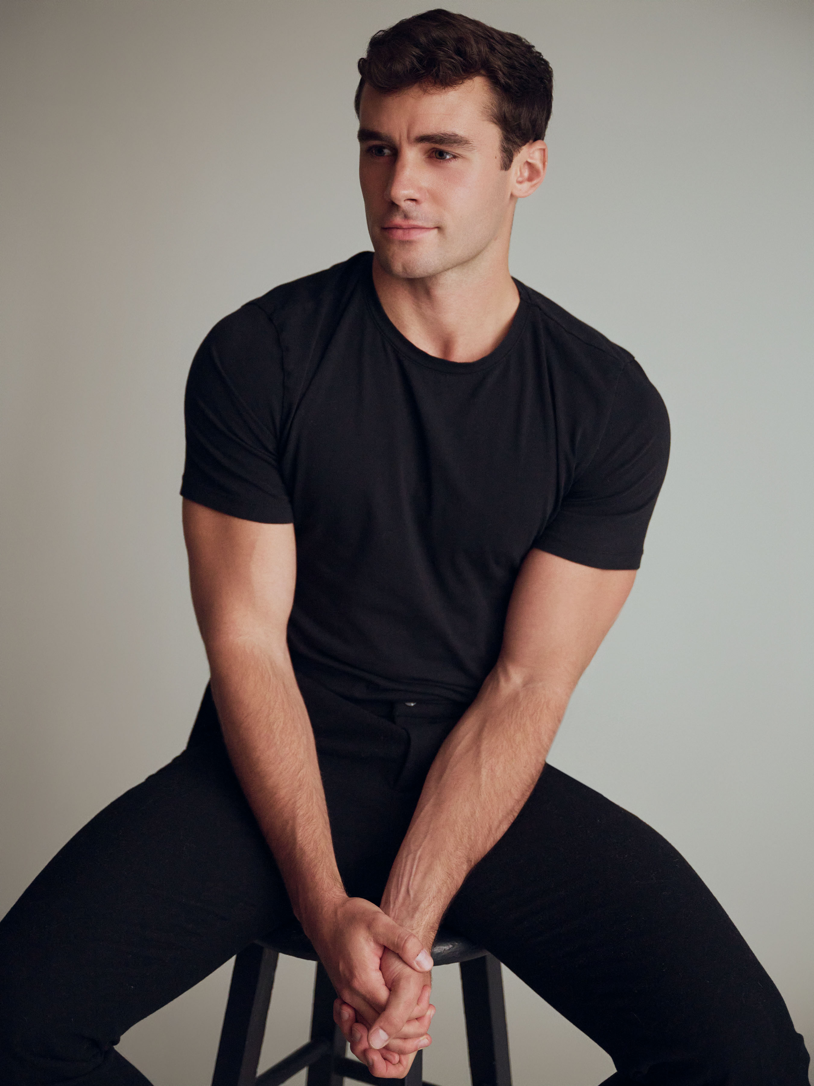 Jake_12_WEB Male model Jake wearing a black t shirt, seated in studio during a professional modeling portfolio shoot